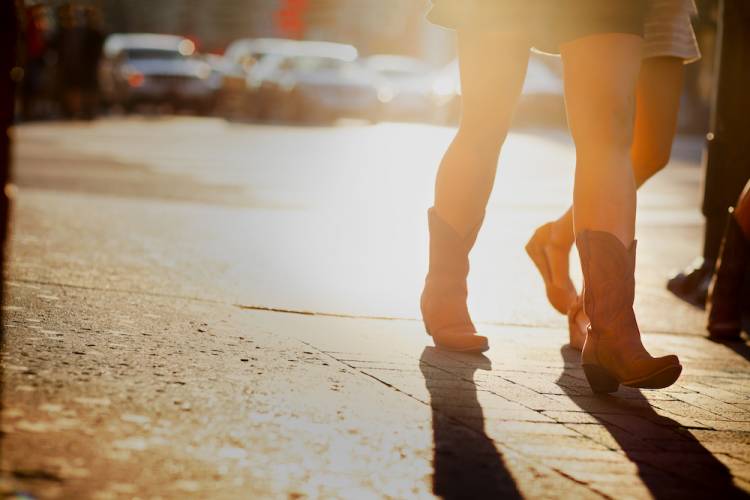 view of legs of woman wearing cowboy boots walking along a street