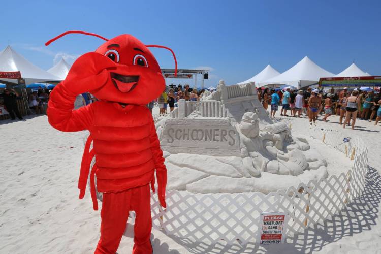 Schooner Restaurant lobster mascot beside a Schooner sand castle on the beach