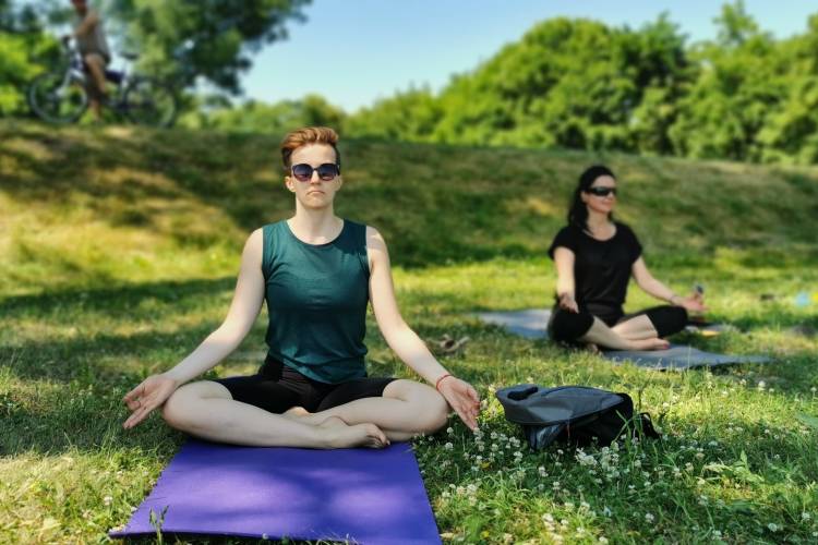 Two women practice meditation on a grassy knoll